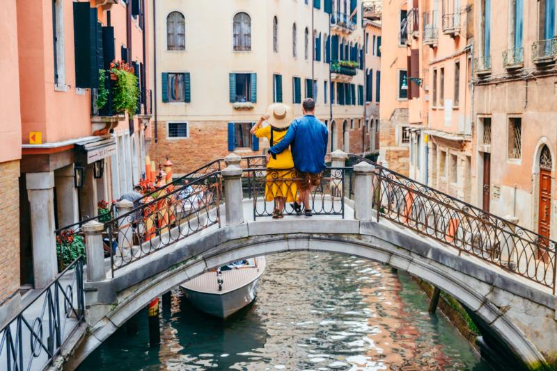 A couple stands on a bridge over a canal in Venice, one of the most romantic cities in the world.