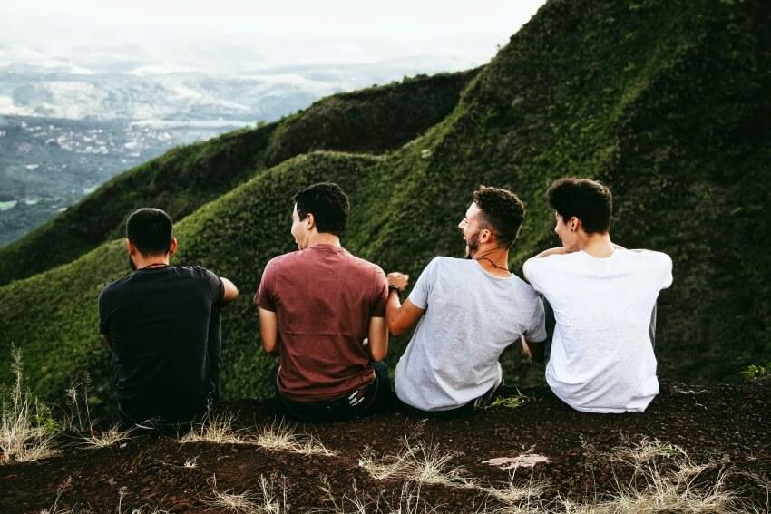 Men Laughing While Sitting and Looking at a Valley