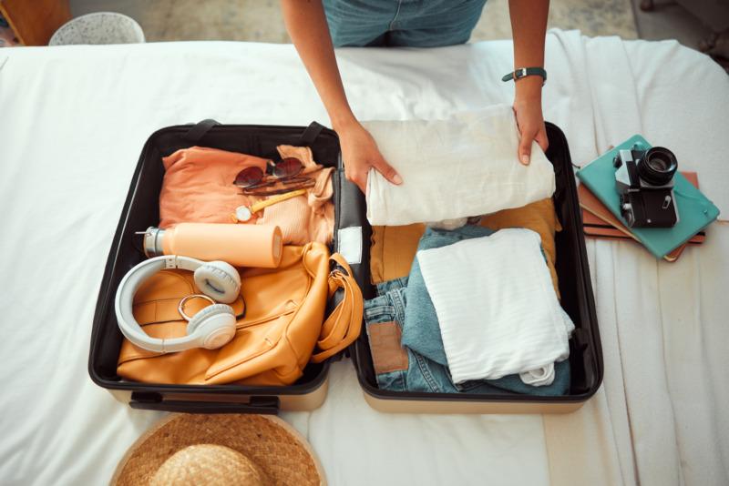 Travel packing, above and hands of a woman with clothes, travel products, and a luggage