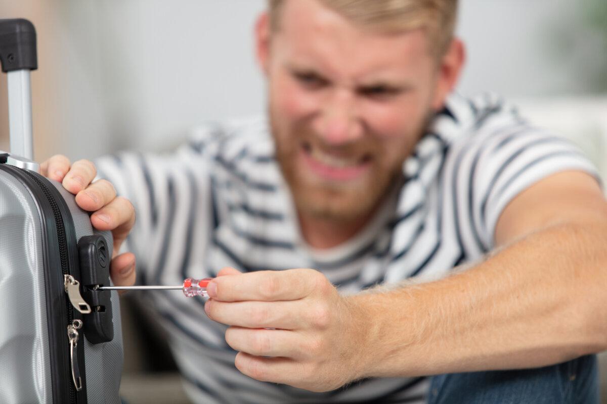 Frustrated man trying to open locked suitcase with screwdriver