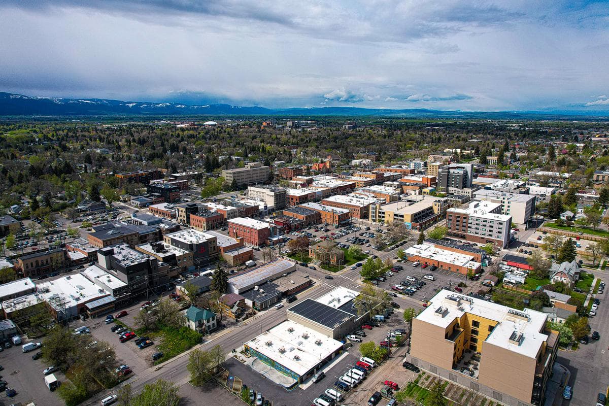 Aerial photo of downtown Bozeman with colorful buildings and natural mountain scenery under a partly cloudy sky.