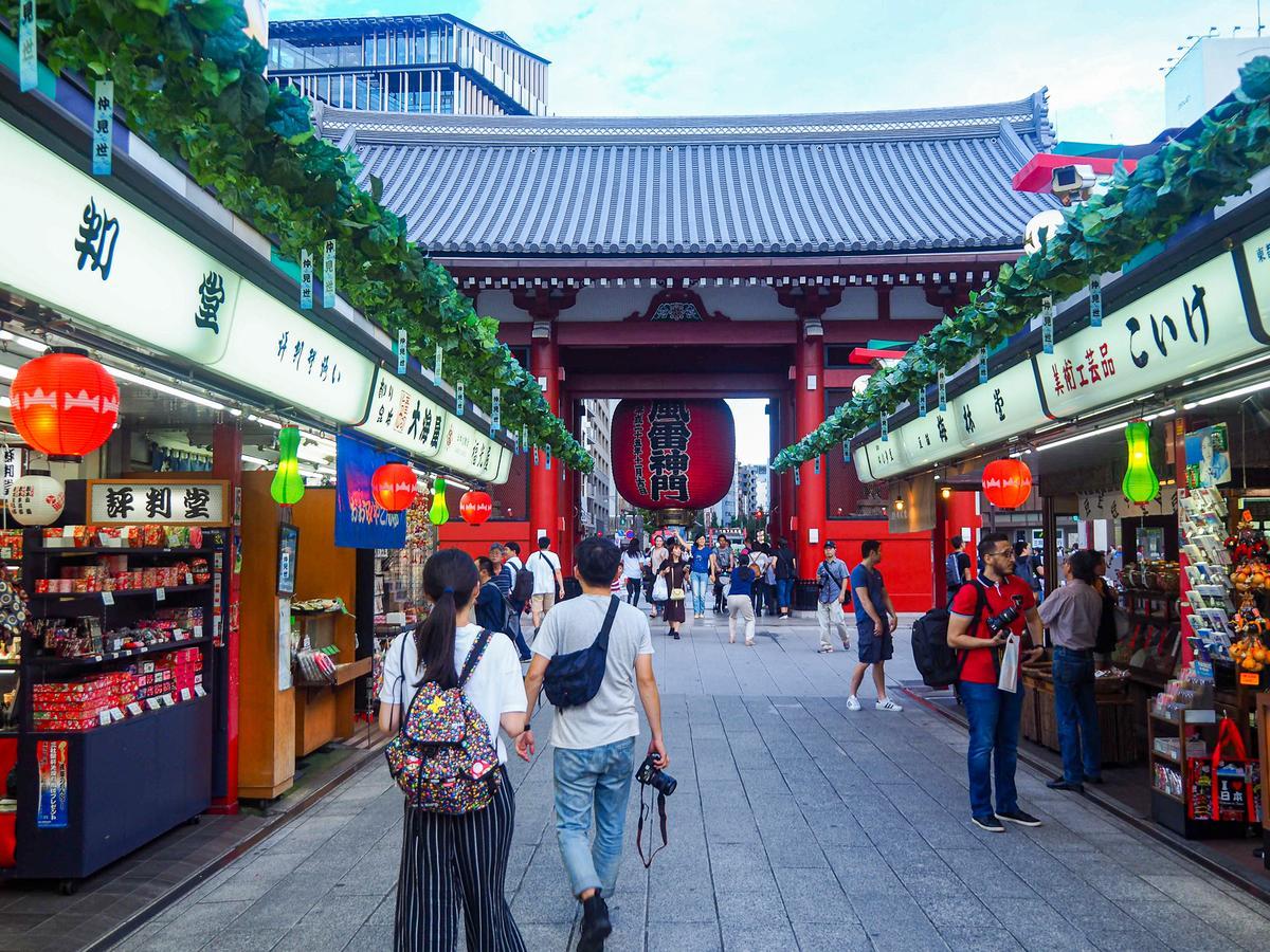 Bustling Nakamise-dori Street in Asakusa, Tokyo with traditional shops, lush vines, and Sensoji Temple gate.