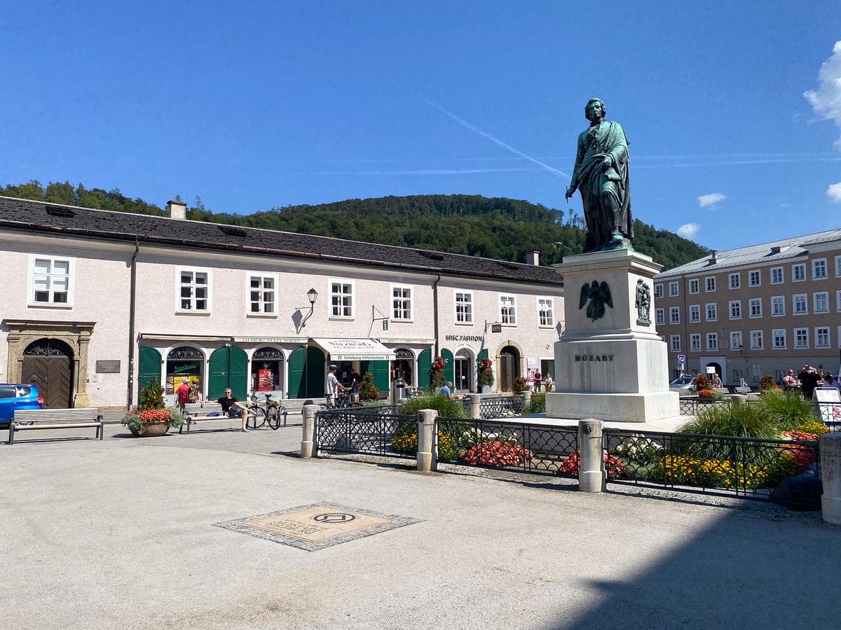 Enchanting Mozart Statue in Salzburg, Austria against clear blue sky with vibrant floral surroundings and historic architecture.