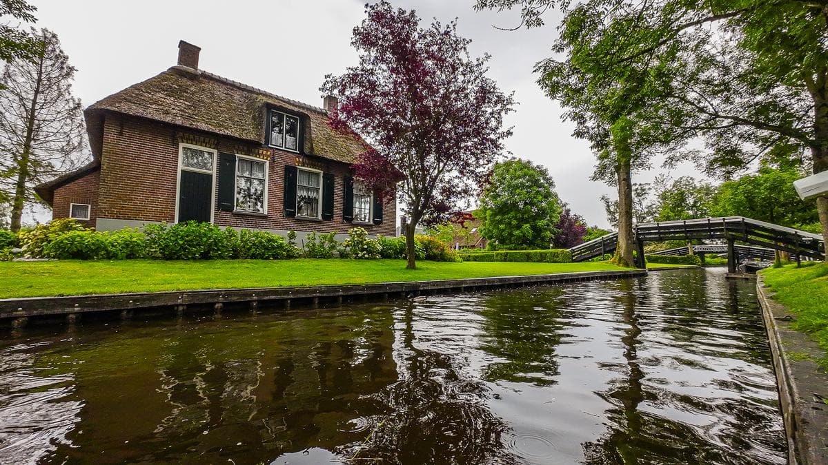 Giethoorn canal cruise with traditional thatched-roof cottage and lush gardens, Netherlands