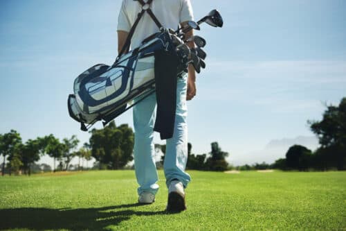 Man on a golf green carrying a bag of golf clubs