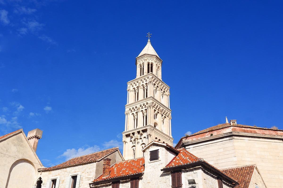 Ancient terracotta-tiled roofs and Romanesque bell tower of Diocletian's Palace set against a pristine azure sky in Split, Croatia.