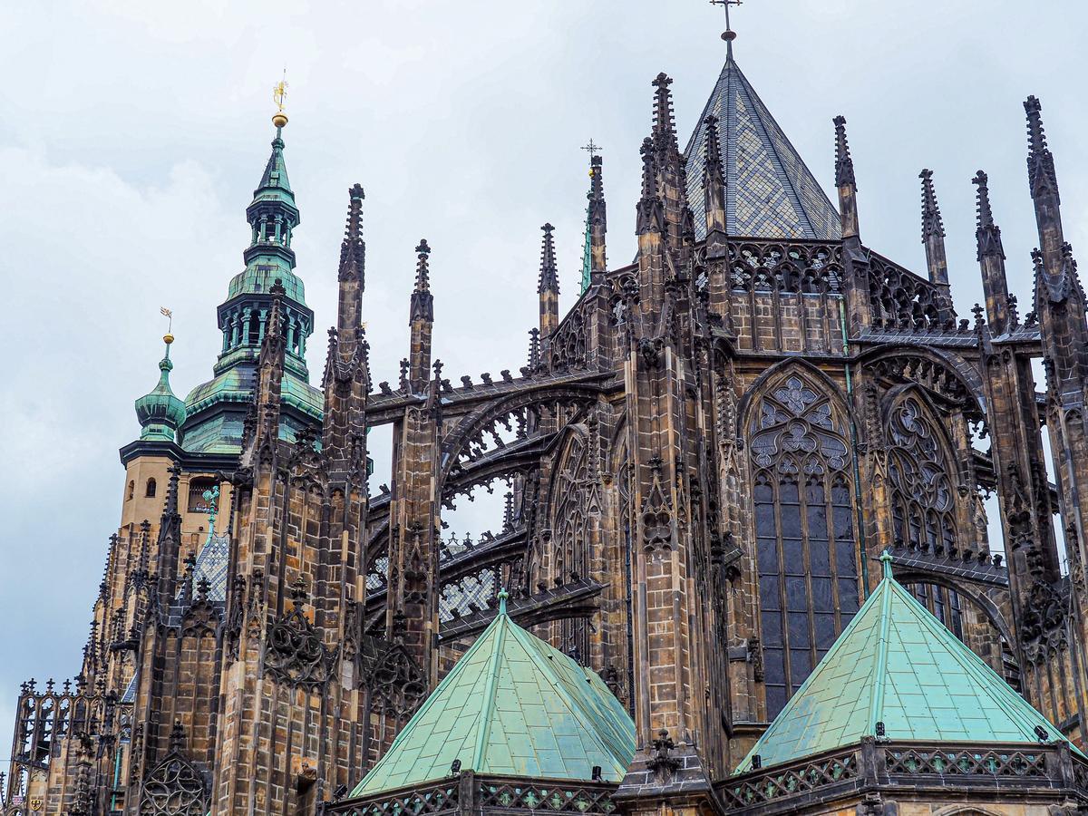 The Gothic spires and architectural details of St. Vitus Cathedral with contrasting turquoise roof under an overcast sky.