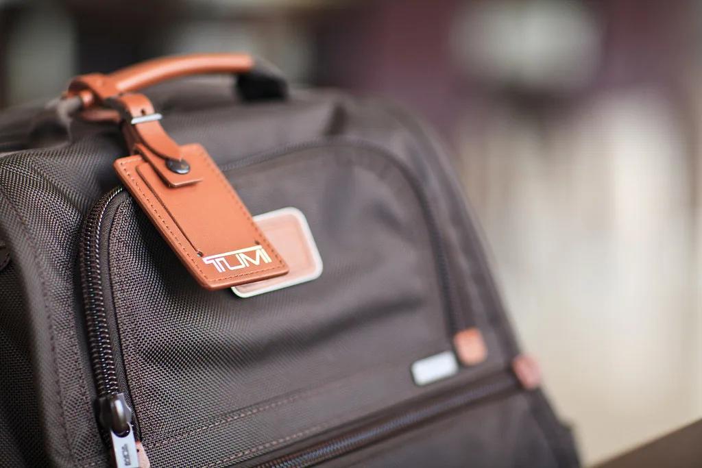 A black TUMI backpack with focus on the brown TUMI luggage tag