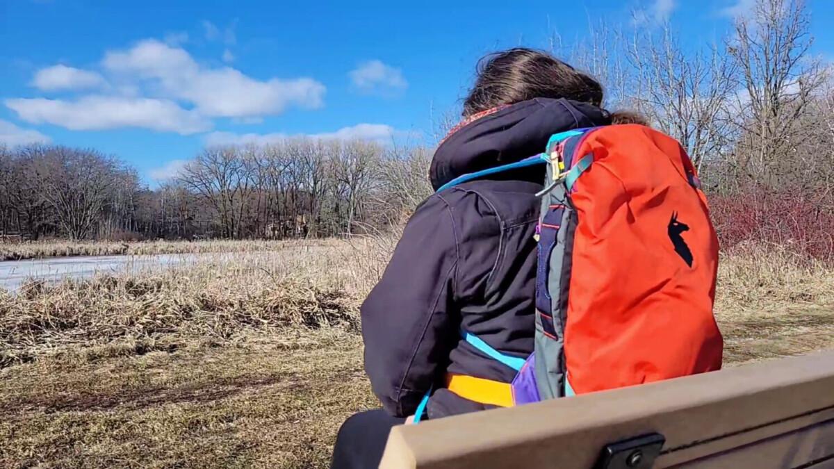 Woman on bench with colorful Cotopaxi backpack outdoors.