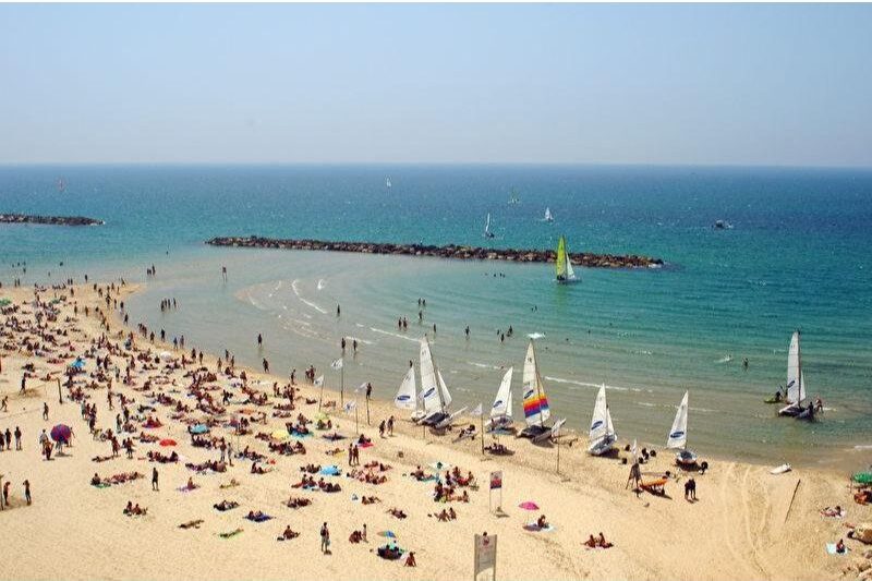 Gordon Beach in Tel Aviv, Israel, vibrant beach scene with sunbathers, sailboats, and colorful umbrellas