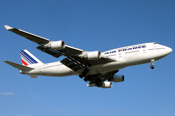 Air France Boeing 747 descends for landing against clear blue sky, landing gear visible.