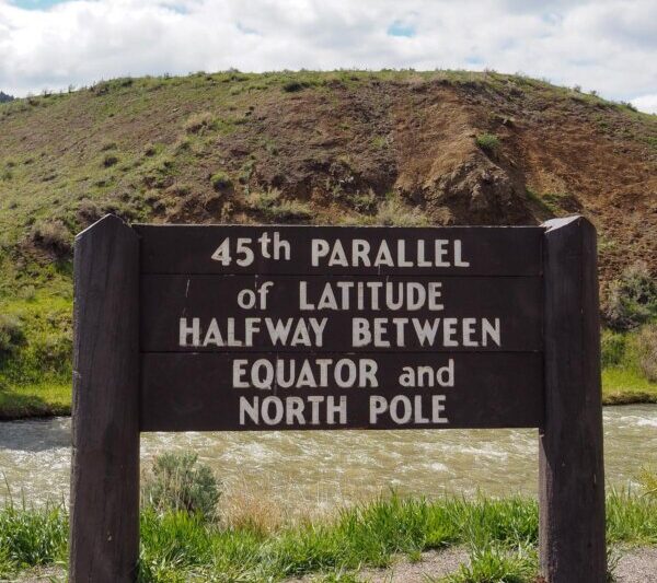45th Parallel latitude marker sign against a scenic hill and river backdrop