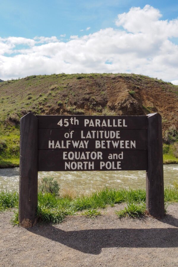 45th Parallel latitude marker sign against a scenic hill and river backdrop