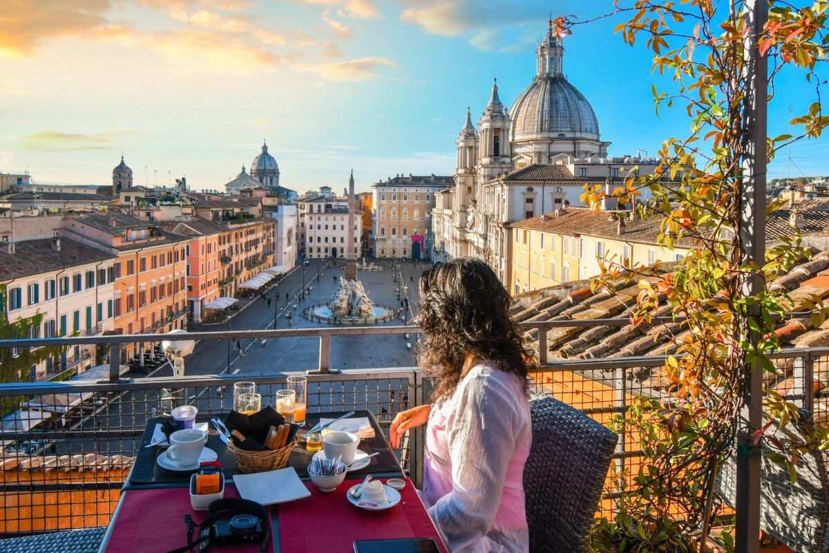 The alt text for this image should be "Woman enjoying a stunning view of Rome, Italy and the Piazza Navona from a rooftop terrace."