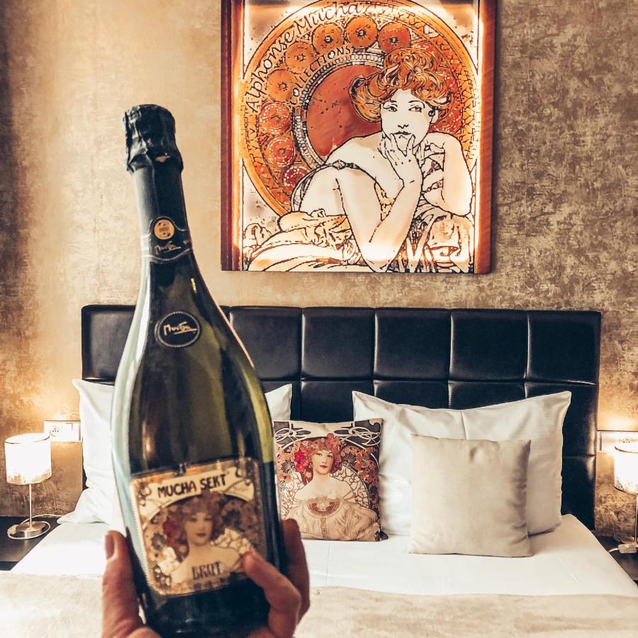 Person holding champagne bottle in front of luxurious bed in dimly lit hotel room.