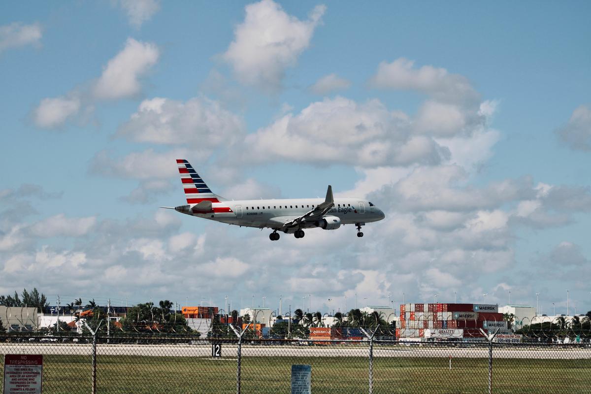 American Airlines plane landing at Miami International Airport with cityscape and containers in the distance.