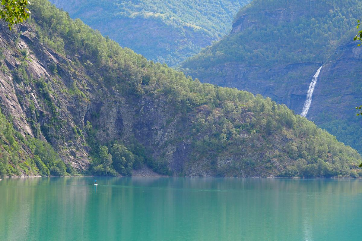 Åsafossen Waterfall cascading by tranquil lake in Skjolden, Norway, surrounded by lush green mountains