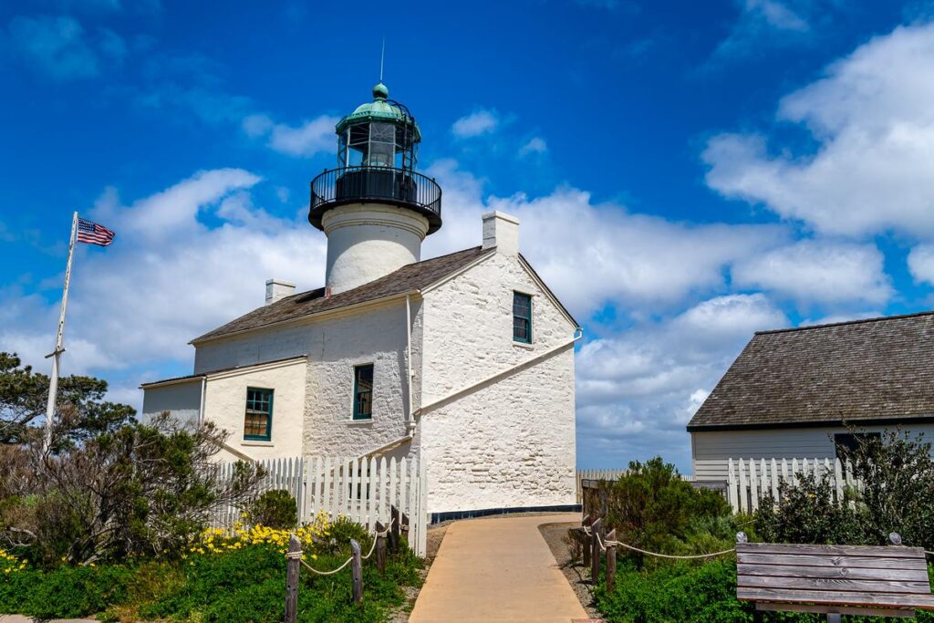 Cabrillo National Monument lighthouse with American flag, clear blue sky, and wildflowers in San Diego.