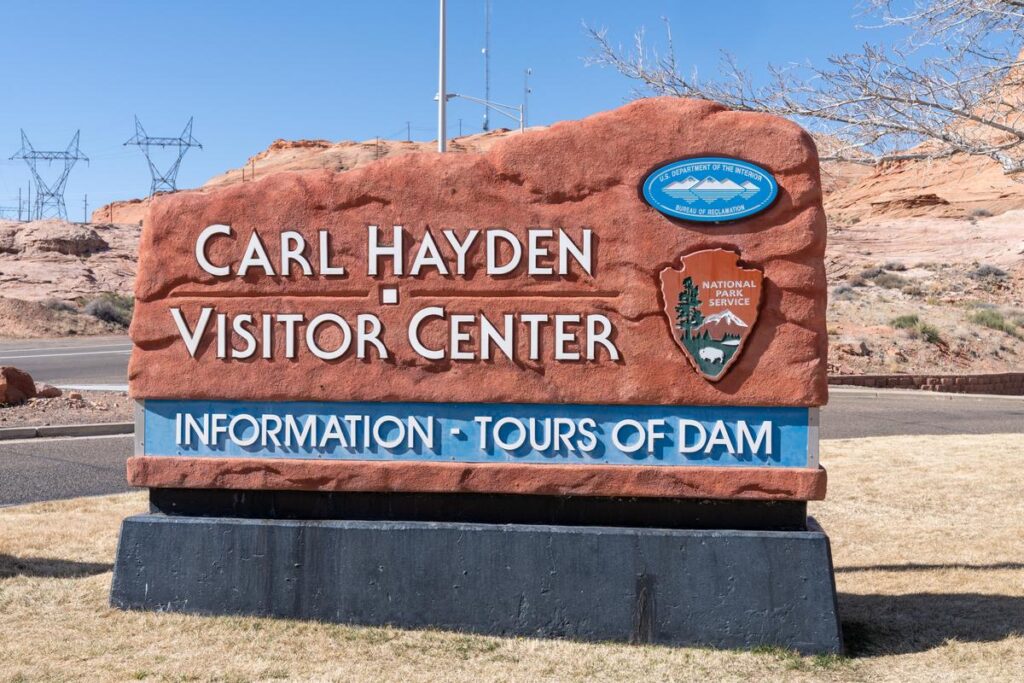 Carl Hayden Visitor Center sign at Glen Canyon Dam with blue sky and desert landscape.
