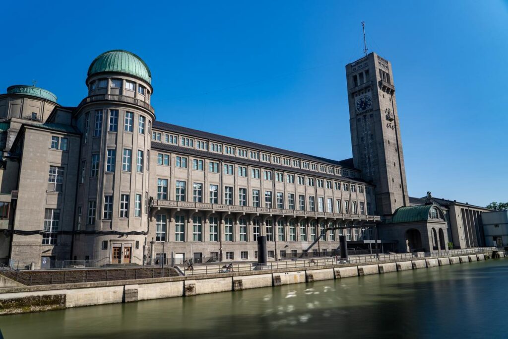 Facade of Deutsches Museum in Munich, iconic architecture with clock tower by the waterfront, clear blue sky.