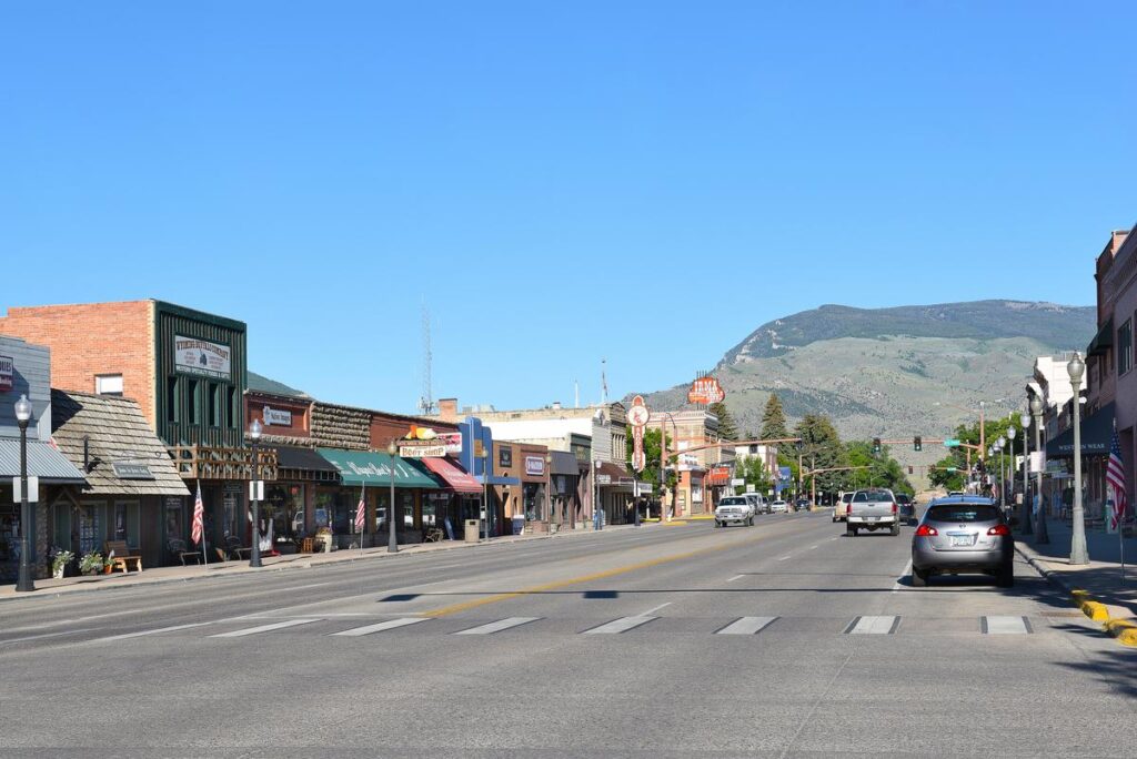 Sunny day on Sheridan Avenue in downtown Cody, Wyoming with historic storefronts and mountain backdrop.