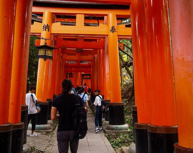 Travelers exploring historic vermilion torii gates of Fushimi Inari Taisha Shrine, Kyoto