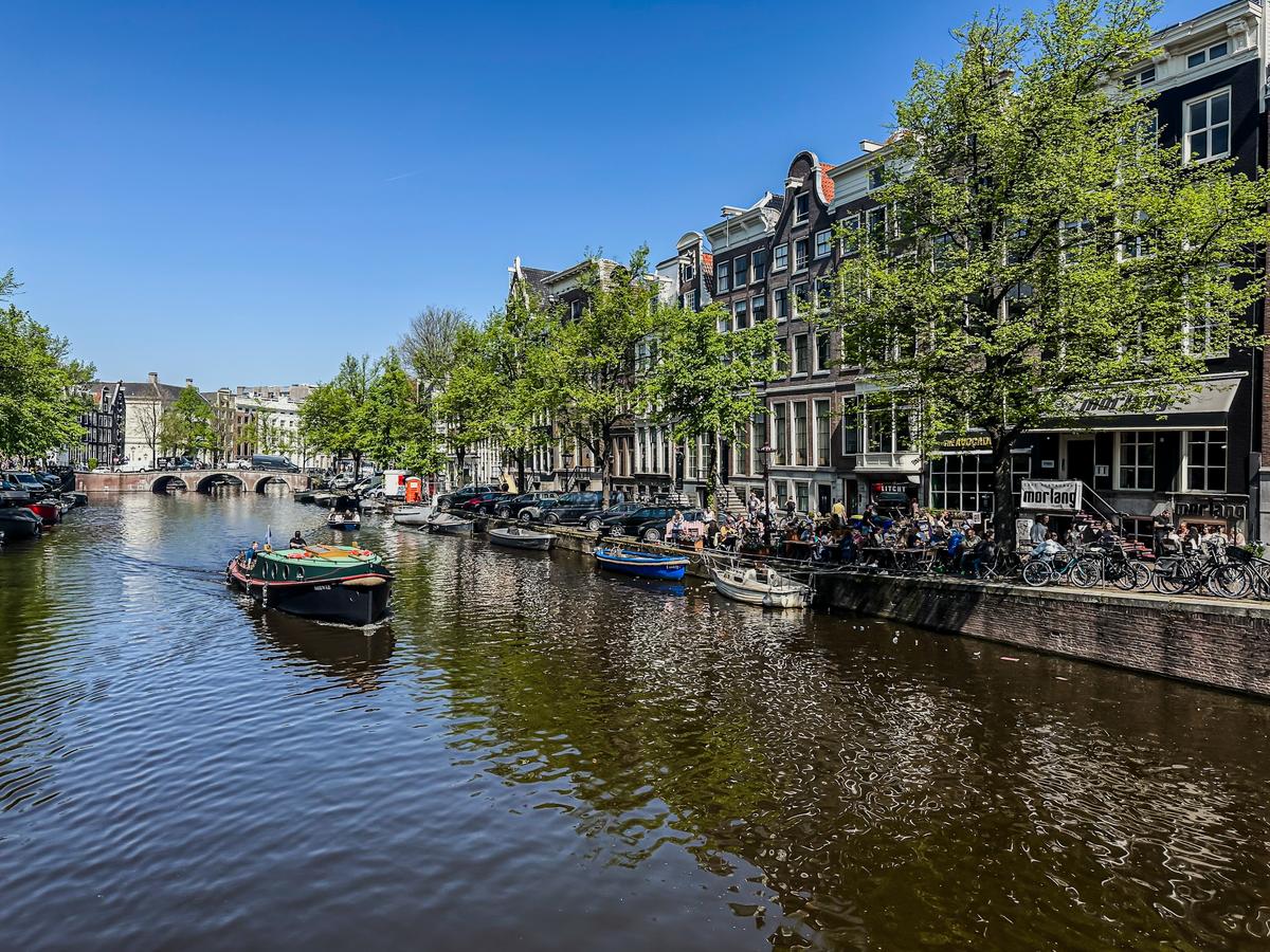 Sunny day at Keizersgracht canal, Amsterdam with boats and lively streets in summer
