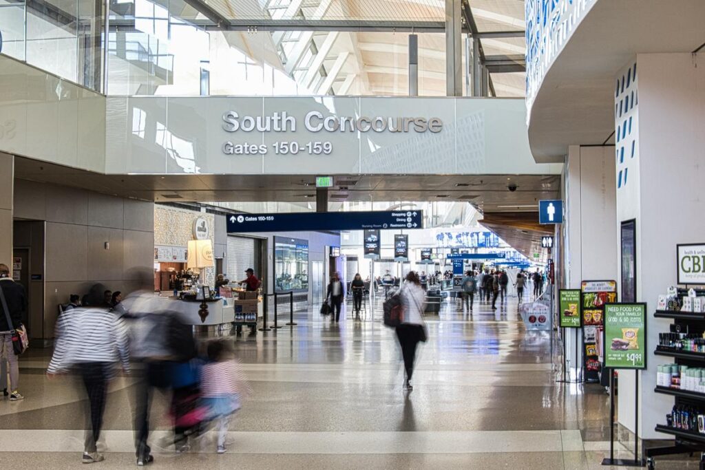 Bustling LAX South Concourse with blurred motion of passengers and directional signage to Gates 150-159.