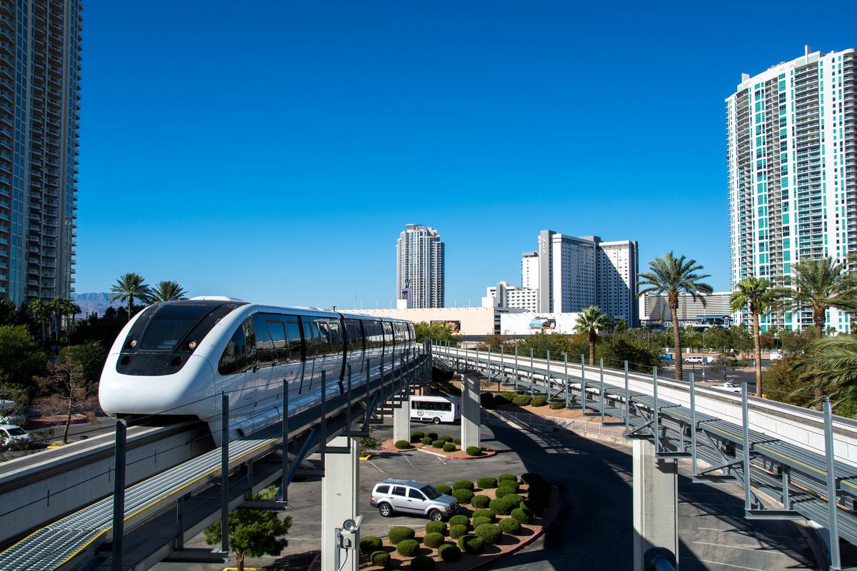 Las Vegas Monorail gliding through the cityscape with high-rises and palm trees under a clear blue sky.