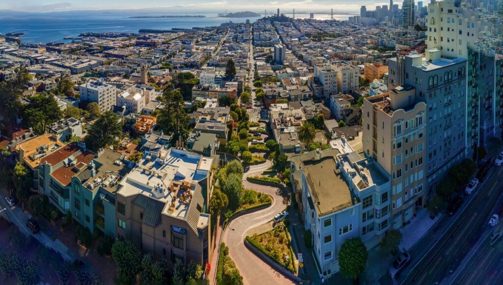 Aerial view of Lombard Street, San Francisco with cityscape and bay in background.