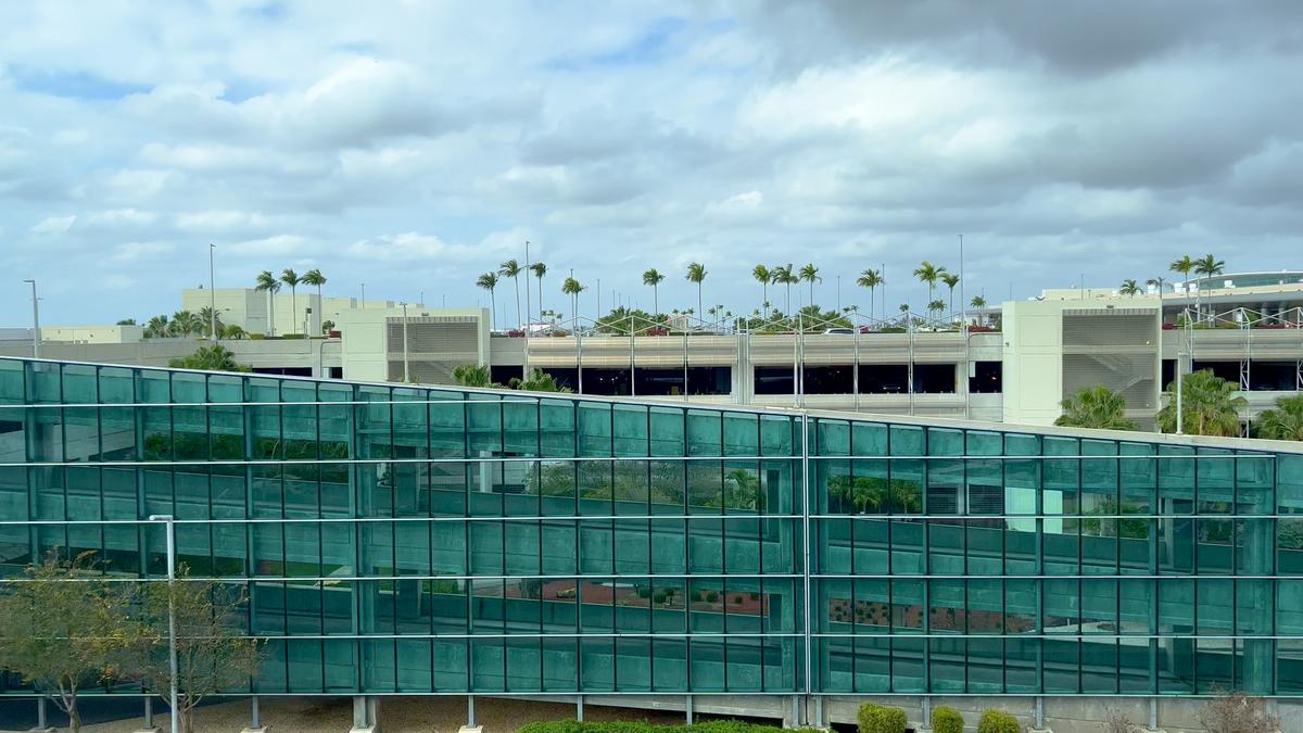 Modern architecture at Miami International Airport, glass-paneled structures, tropical palm trees, partly cloudy sky.