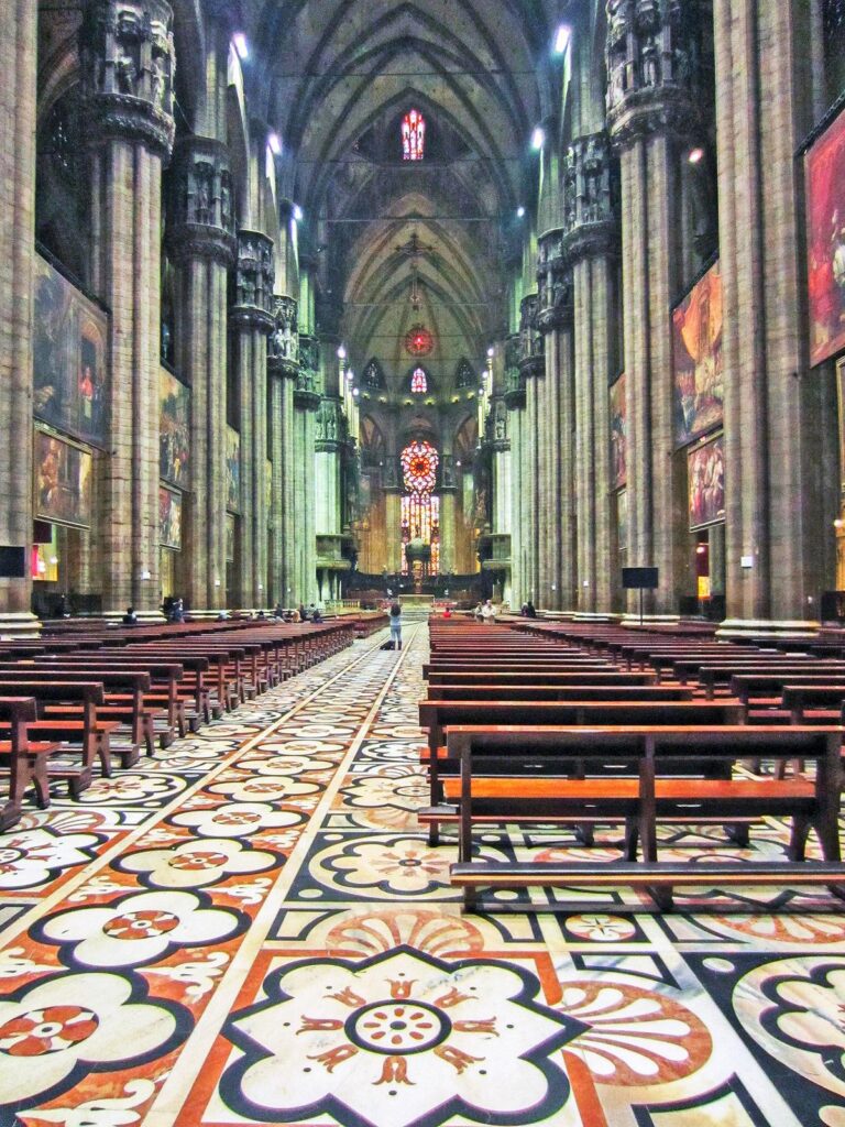 Milan Cathedral interior with Gothic architecture, stained glass, and floor tiles.