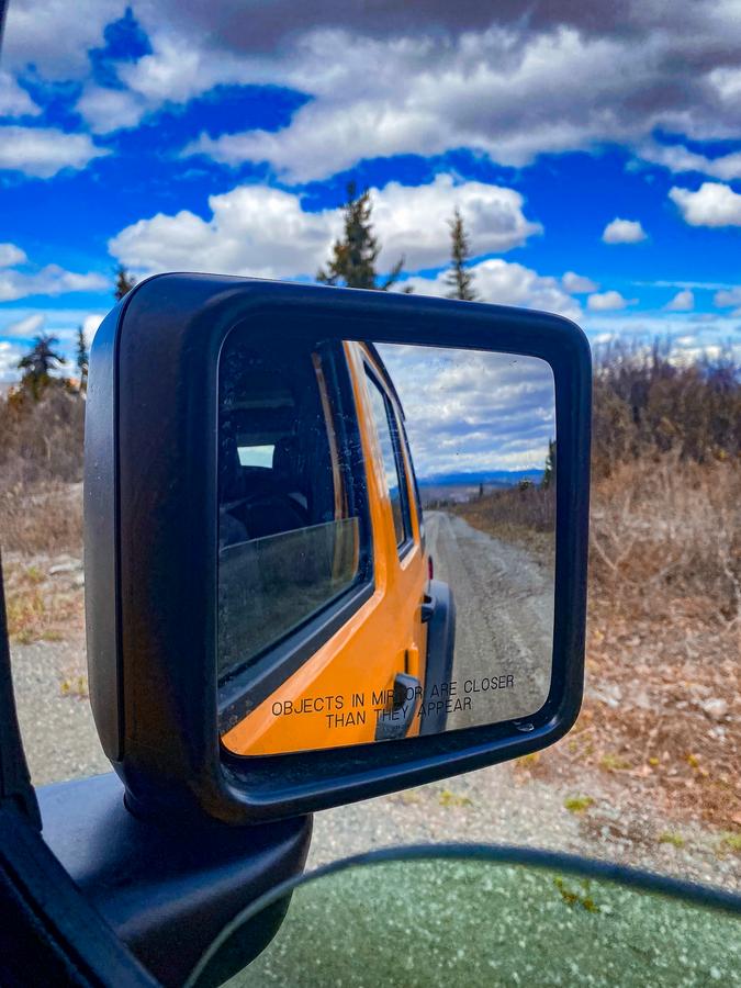 Rear-view mirror reflection during scenic Denali jeep tour under vibrant skies