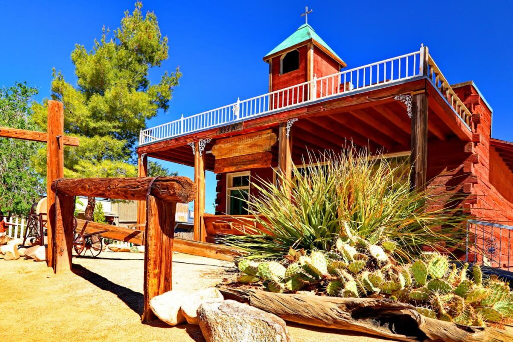 Sunny day at historic Pioneertown chapel with rustic wooden architecture and vibrant desert plants.