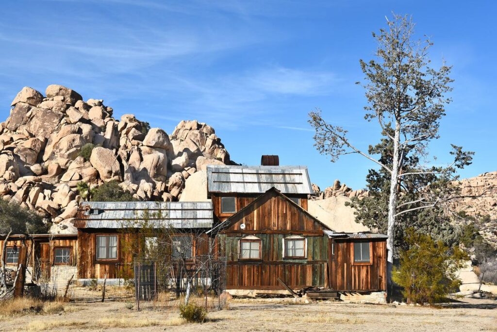 Historic Keys Ranch in Joshua Tree National Park, rustic wooden buildings against rock formations and blue sky.