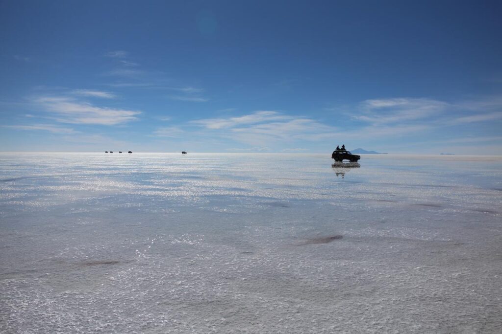 Tour vehicles crossing the reflective Salar de Uyuni, Bolivia under a clear blue sky.