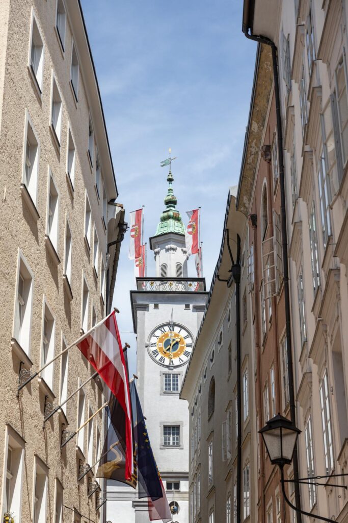 Salzburg Old Town Hall tower with clock and European flags against clear sky, historic architecture in Austria.
