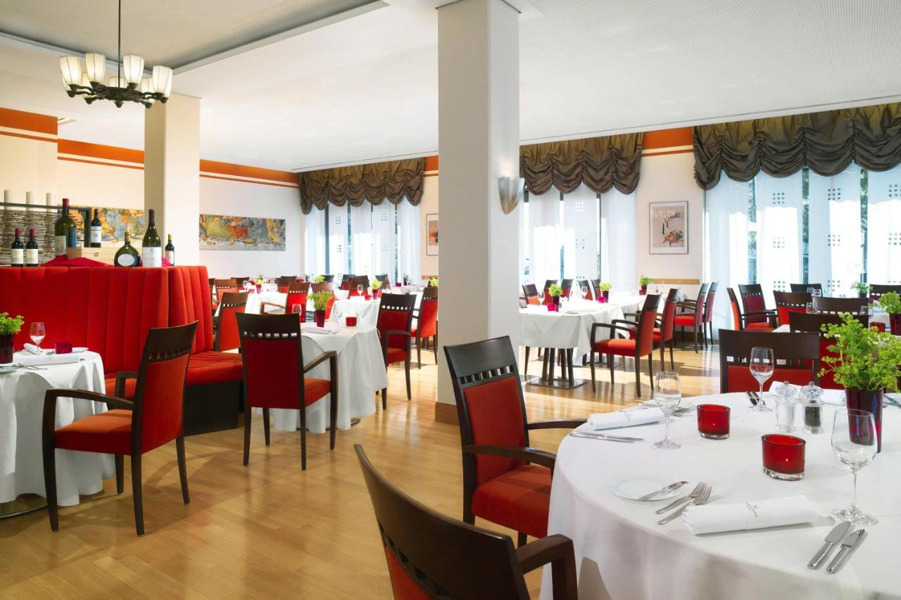 Elegant dining room at Sheraton Carlton Hotel Nuremberg with white tablecloths, silverware, and warm lighting.