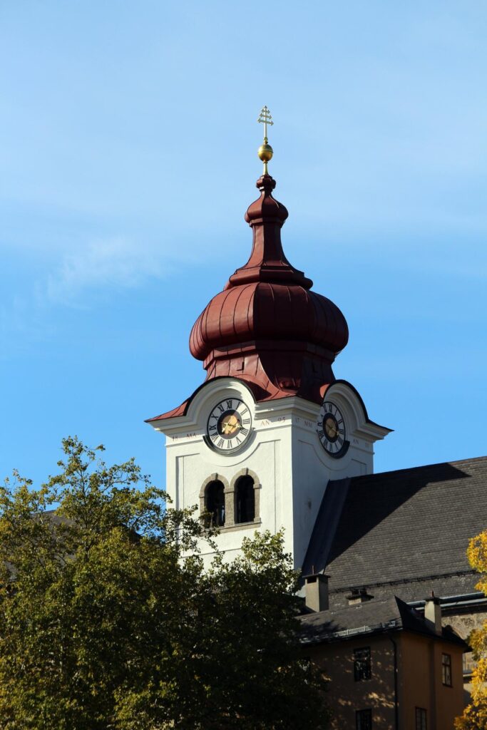 Baroque-style clock tower with red dome and golden cross, Stift Nonnberg Abbey, autumn.