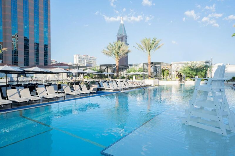 Luxurious swimming pool at The Venetian Las Vegas with a towering modern building in the background and lush greenery around.