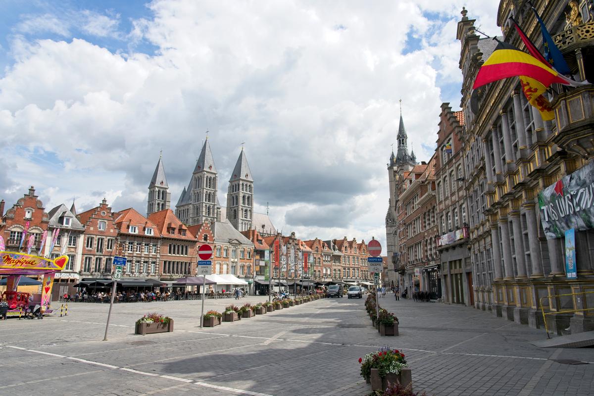 Tournai, Belgium cityscape with medieval architecture, vibrant flags, and cobblestone square under a cloudy sky.