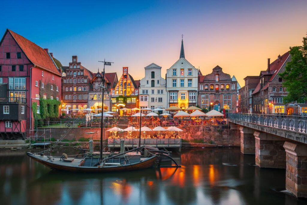 Twilight view of Stintmarkt in Lüneburg with historic buildings, waterfront dining, and boat.