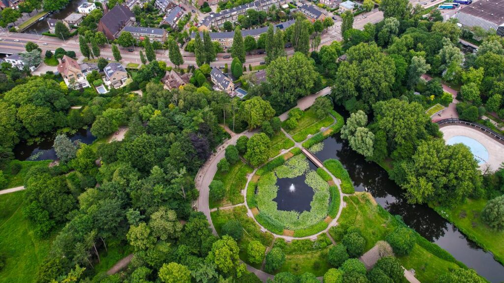 Aerial view of Beatrixpark with winding paths, lawns, and a pond beside the Zuidas
