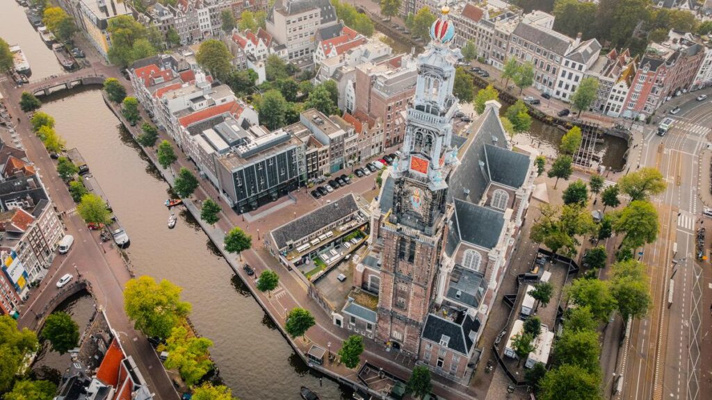 Aerial view of historic Westerkerk and Amsterdam canals with boats and Dutch architecture.