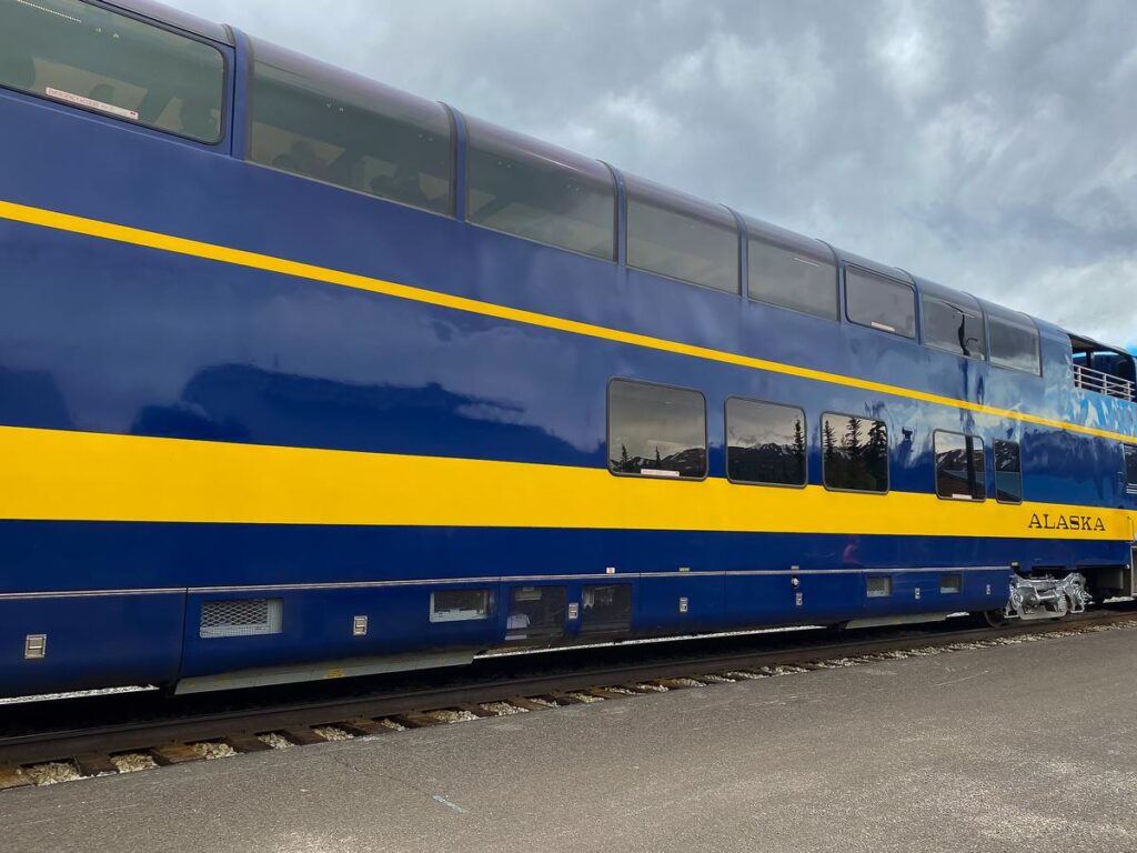 Vibrant blue and yellow Alaska Railroad passenger train car with scenic reflections in Alaskan wilderness