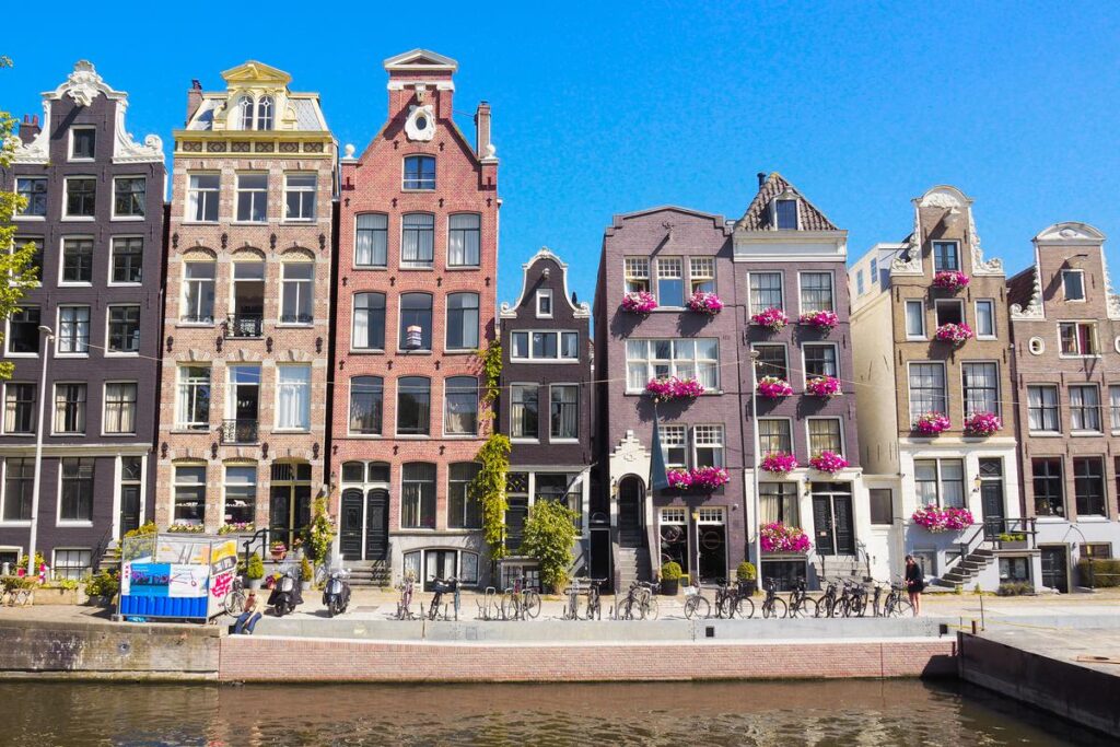 Amsterdam canal houses with bright flowers under a blue sky