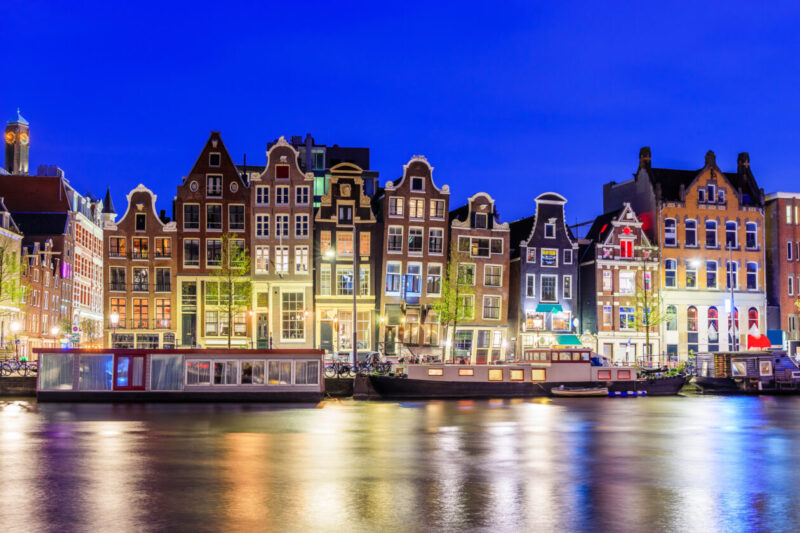 Amsterdams colorful dancing houses along Damrak canal at twilight with reflections.