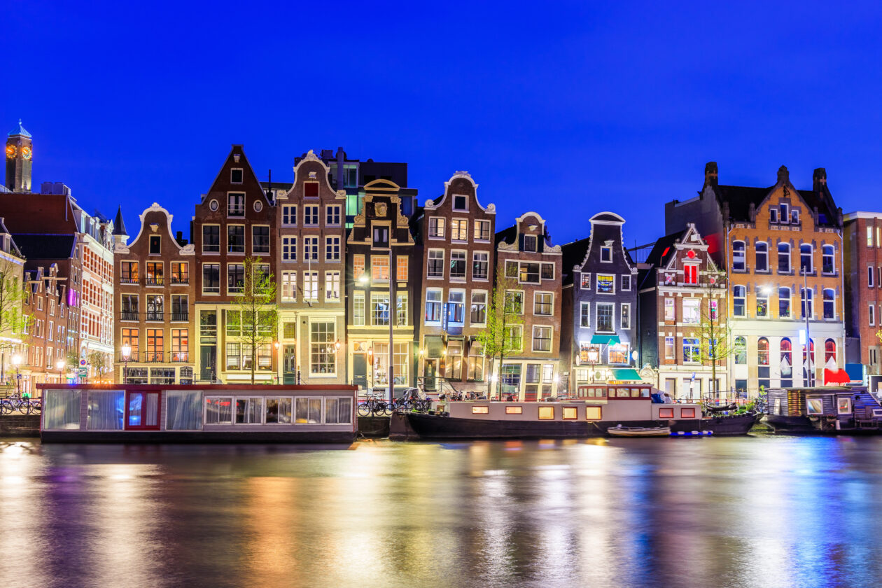 Amsterdams colorful dancing houses along Damrak canal at twilight with reflections.