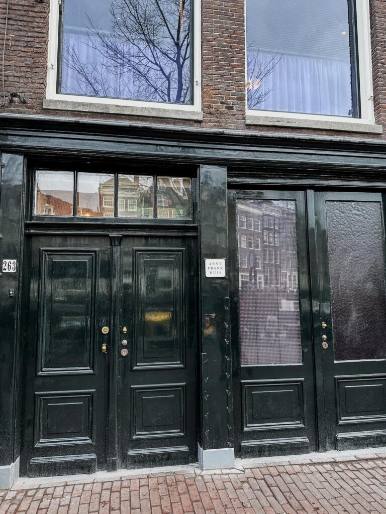 Exterior view of Anne Frank House in Amsterdam, with signature black facade and green entry doors, museum plaque by entrance.