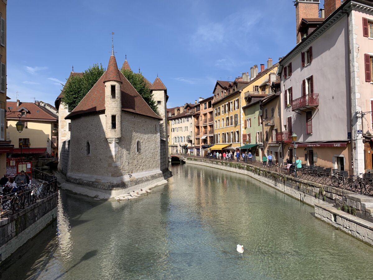 The alt text for the image should be "Cityscape with river in vibrant Annecy, France."